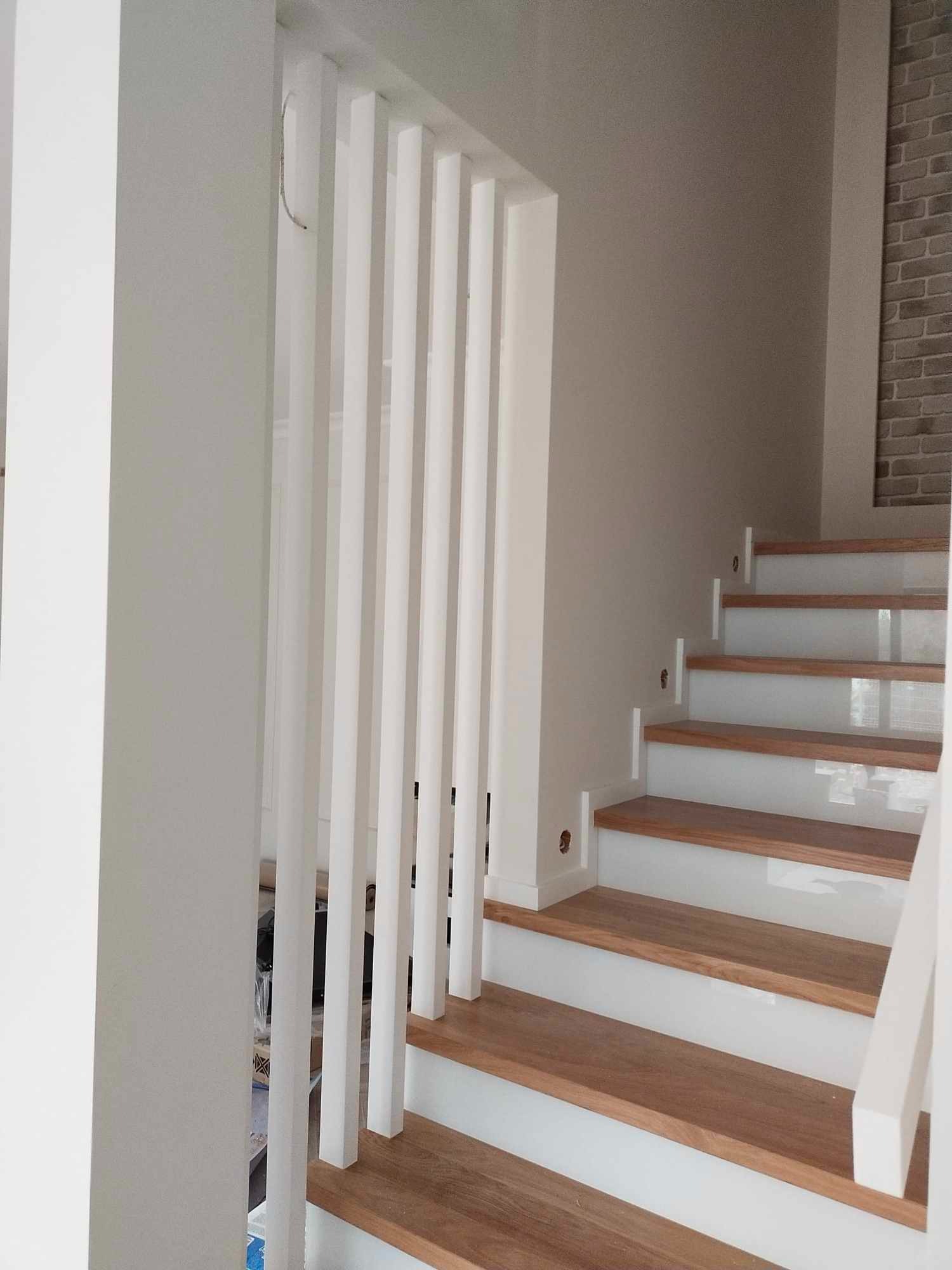 Nowoczesne schody z drewnianymi stopniami i białymi podstopnicami, z pionowymi białymi elementami balustrady, widok z dołu.