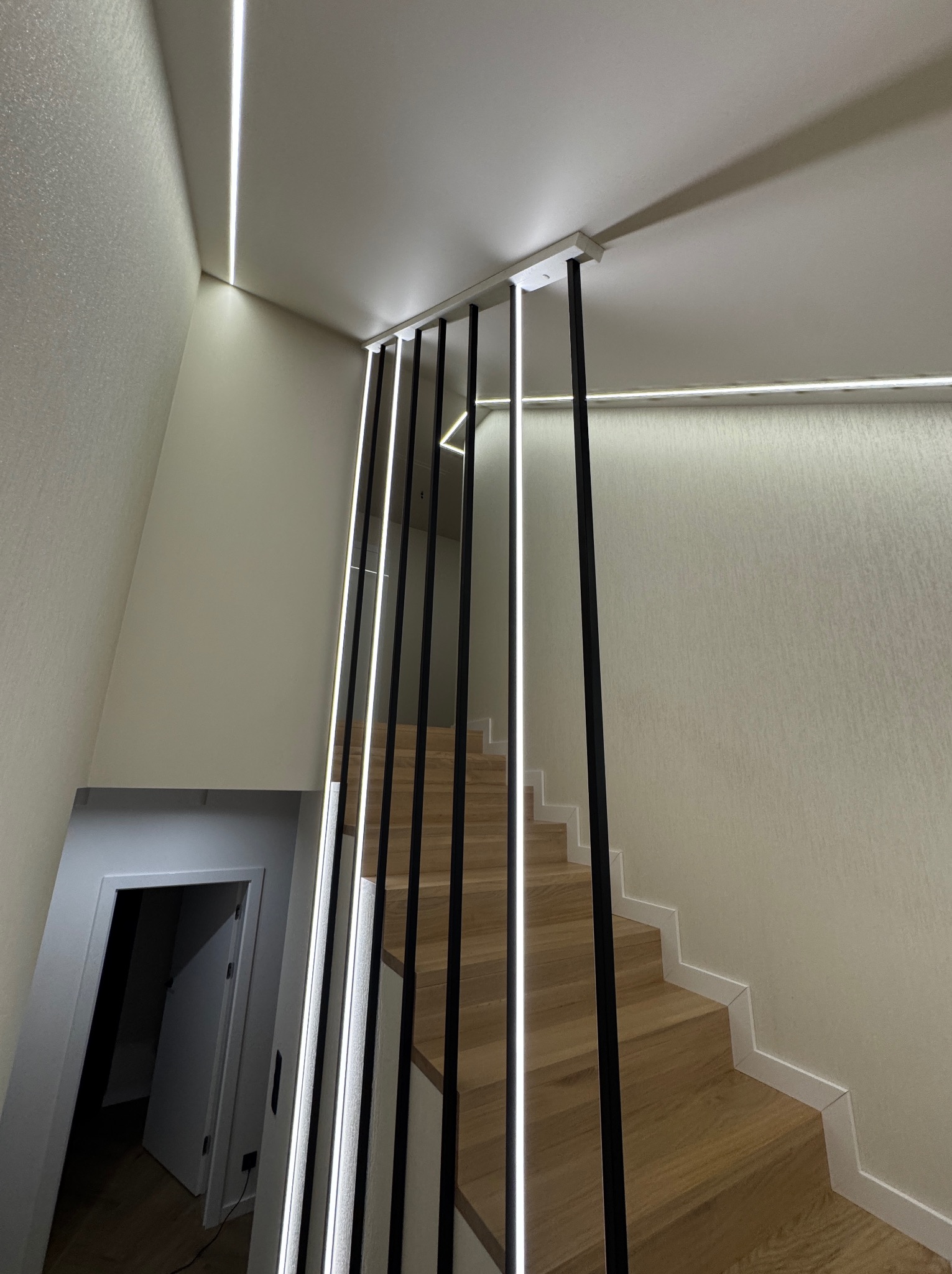 Nowoczesne oświetlenie schodów z czarnymi balustradami i liniowymi lampami LED wzdłuż stopni i sufitu, tworzące minimalistyczny design wnętrza.