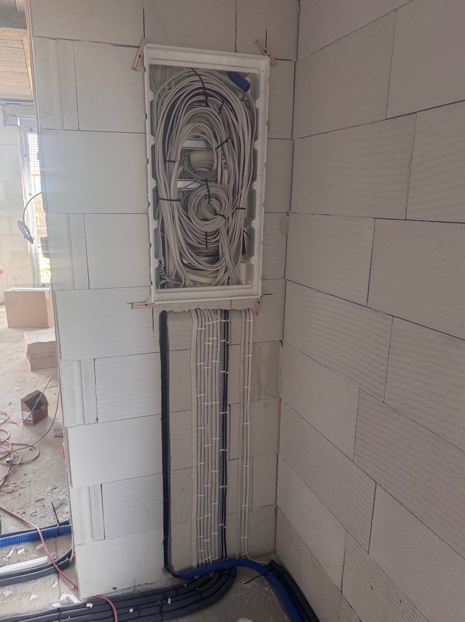 Rozdzielnia elektryczna w ścianie z betonu komórkowego, widoczne kable w peszlach i puszce. Instalacja w trakcie montażu, surowy stan.