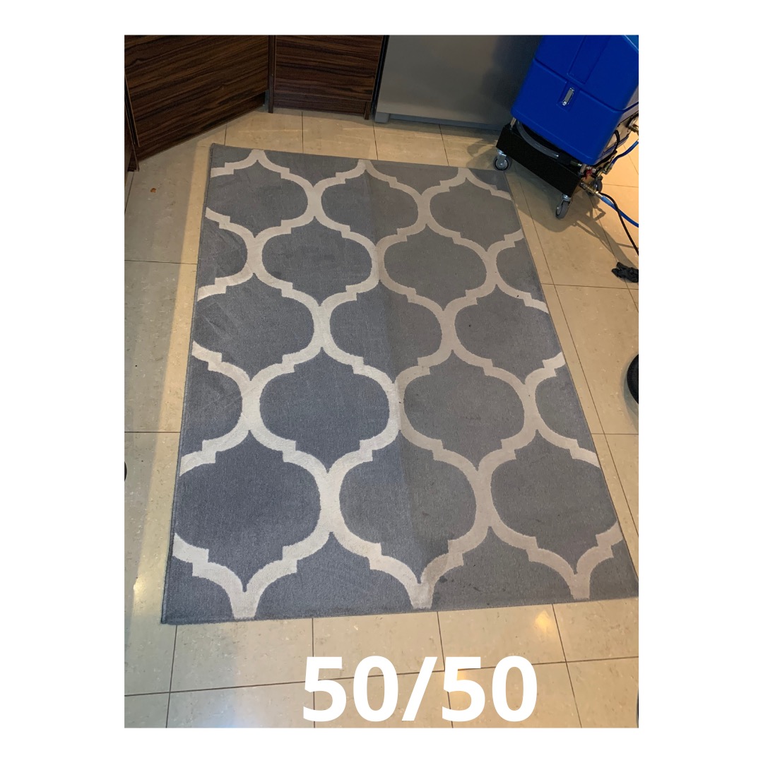 Szary dywan z białym wzorem marokańskim leżący na podłodze z płytkami, obok stoi niebieski odkurzacz piorący.