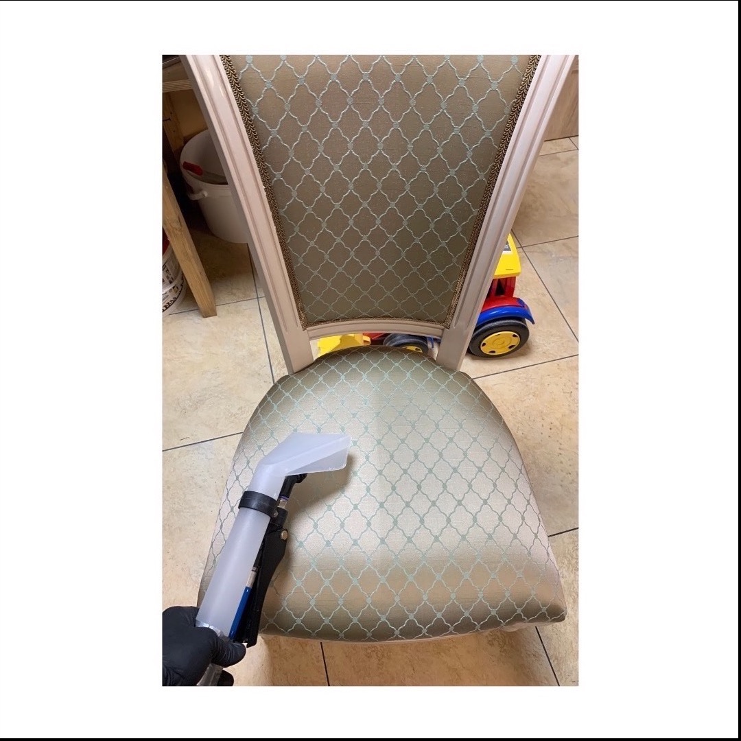Czyszczenie tapicerki krzesła z wzorem, widoczna dysza urządzenia czyszczącego i fragment dziecięcej zabawki w tle.
