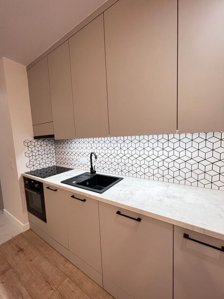 Nowoczesna kuchnia z beżowymi frontami, czarnym zlewem i armaturą oraz geometryczną mozaiką na ścianie.