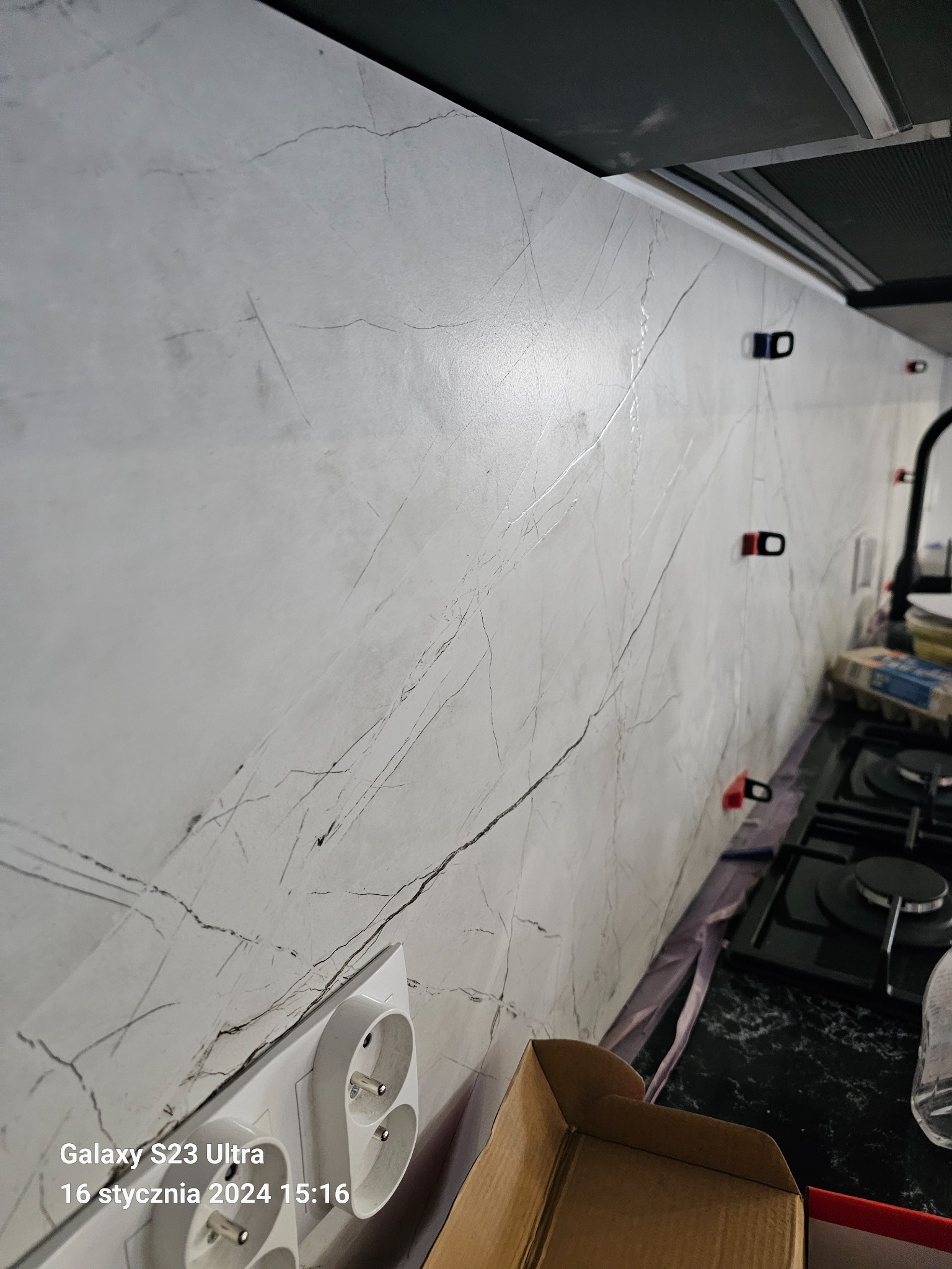 Ściana w kuchni wykończona płytami imitującymi marmur, z widocznymi gniazdkami elektrycznymi i systemem poziomowania płytek podczas montażu.