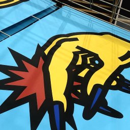 NO.REP - Świeżo wydrukowane, jaskrawe naklejki z żółto-czarno-czerwonym motywem ręki i wybuchu na błękitnym tle, ułożone w metalowej siatce.