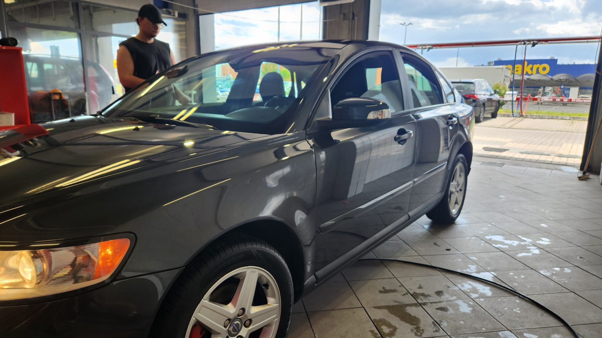 Ciemnoszary samochód osobowy po umyciu w myjni w Zabrzu, widoczny pracownik wycierający karoserię, w tle budynek sklepu.