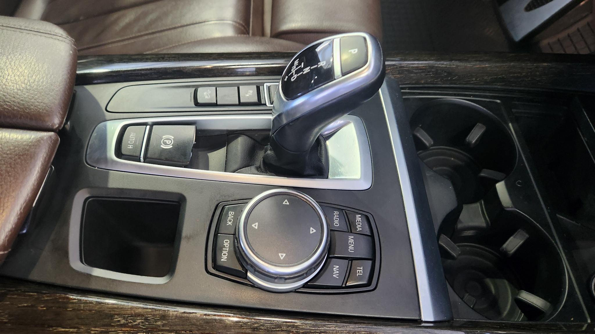 Wnętrze samochodu z widocznym tunelem środkowym, dźwignią zmiany biegów w pozycji parkowania, panelem sterowania multimediami i uchwytami na napoje.