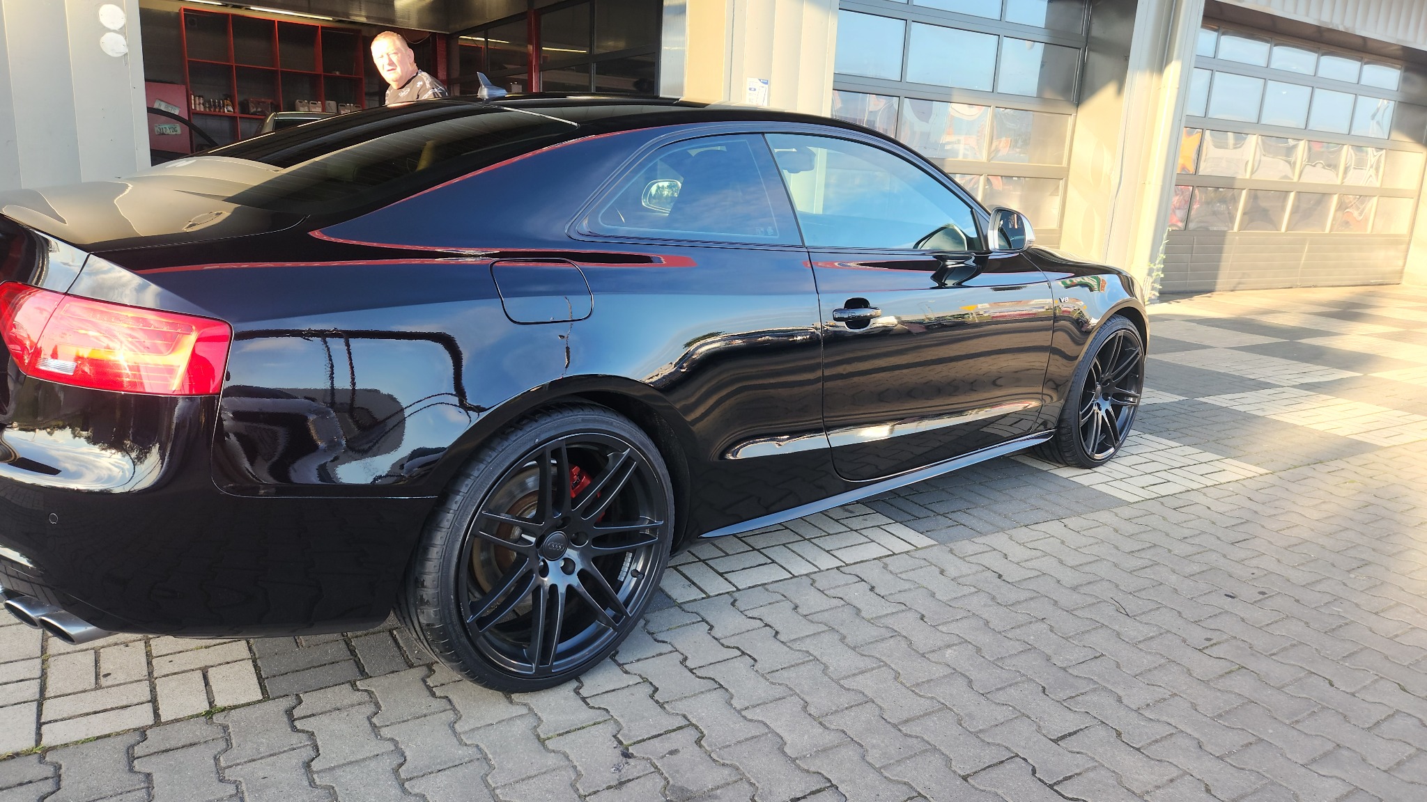 Błyszczący, czarny samochód marki Audi po umyciu w myjni w Zabrzu, widoczne detale karoserii i felgi. Na karoserii widoczne odbicia otoczenia.
