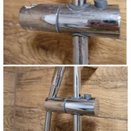 Błyszcząca, chromowana bateria prysznicowa z szarym pokrętłem na tle drewnopodobnych płytek ściennych.