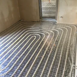 Montaż ogrzewania podłogowego w trakcie realizacji w pomieszczeniu w Budziszewicach, widoczne rury grzewcze ułożone na folii z siatką.