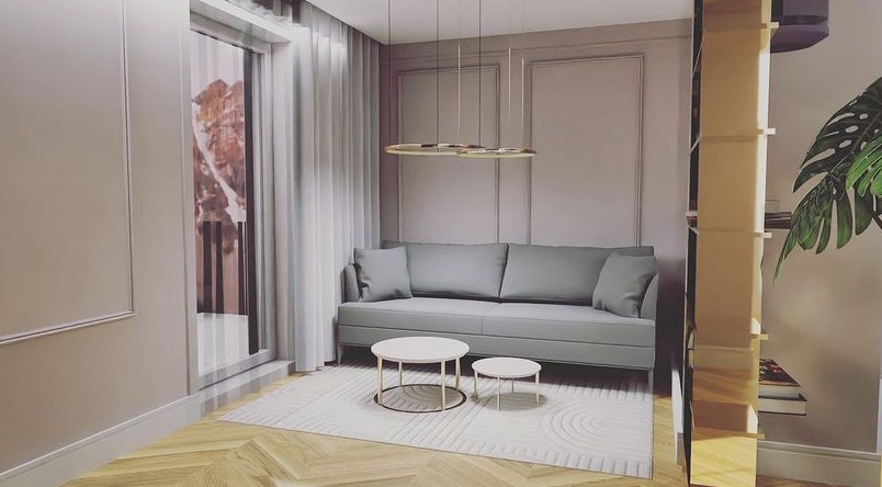 Jasnoszary salon z sofą, dwoma okrągłymi stolikami kawowymi na wzorzystym dywanie, wiszącą lampą pierścieniową i regałem z książkami, uzupełniony rośliną doniczkową.