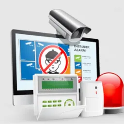 Komputer z ekranem prezentującym schemat monitoringu z kamerami i przekreślonym wizerunkiem złodzieja, panel sterowania alarmem, czujnik ruchu i czerwona lampa alarmowa.