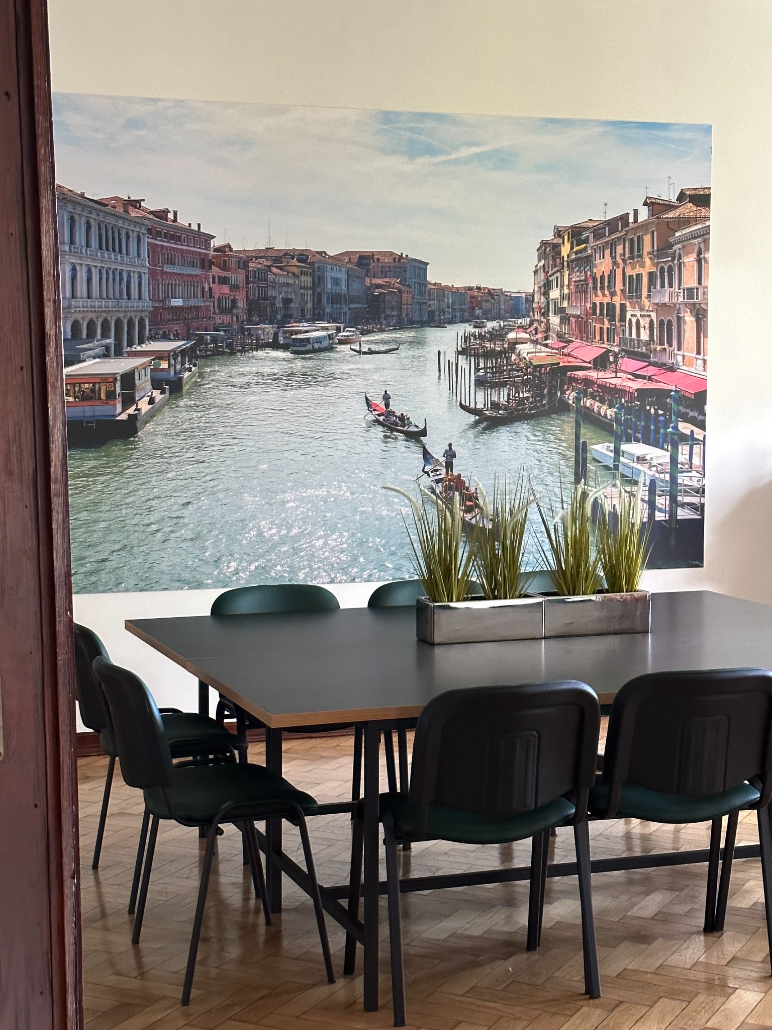 Sala konferencyjna z dużym fototapetą przedstawiającą wenecki kanał, na stole metalowa donica z trawami ozdobnymi.