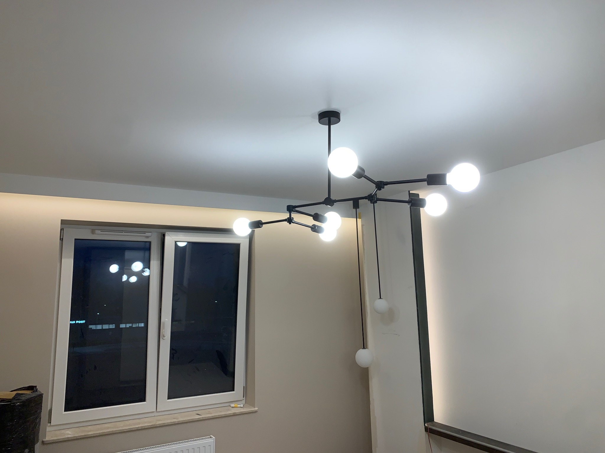 Czarna, nowoczesna lampa sufitowa z kulistymi, mlecznymi żarówkami, zainstalowana w jasnym pomieszczeniu z oknem i minimalistycznym wystrojem.