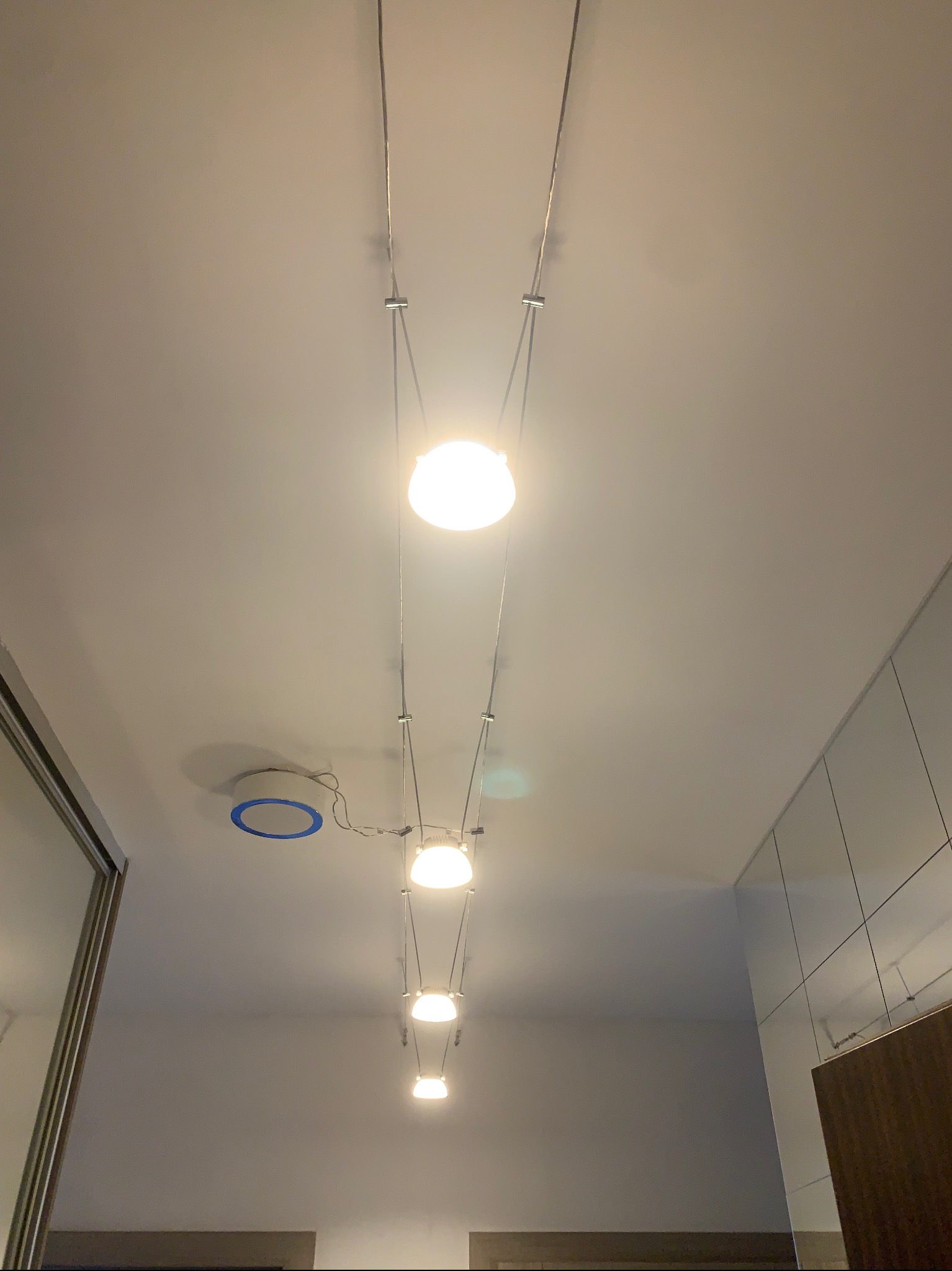 Szereg kulistych lamp wiszących na cienkich linkach, rozmieszczonych wzdłuż sufitu, widoczny także okrągły plafon z niebieskim akcentem.