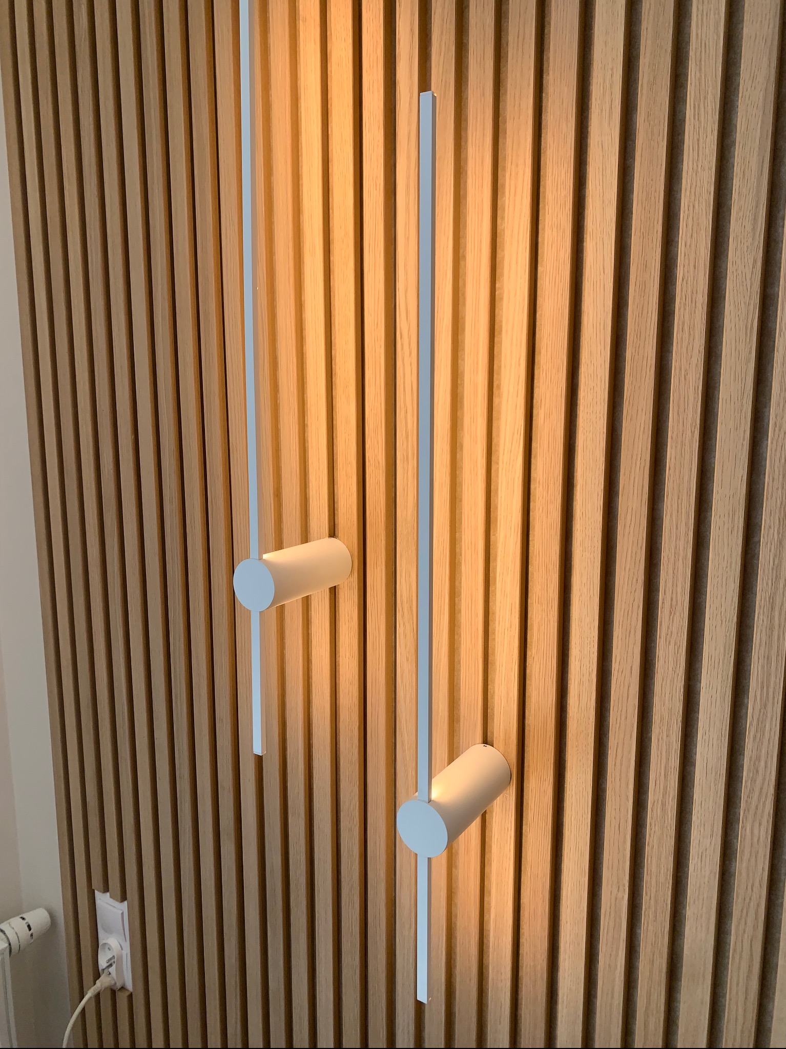 Nowoczesne oświetlenie ścienne z cylindrycznymi lampami na tle drewnianej ściany z lameli. Ciepłe światło podkreśla strukturę drewna.