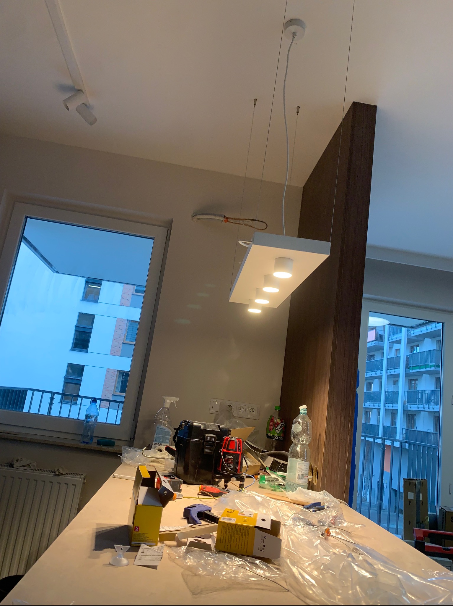 Nowoczesna, biała lampa sufitowa z sześcioma punktami świetlnymi, zawieszona nad blatem roboczym w trakcie montażu, z widocznymi narzędziami i elementami instalacji.