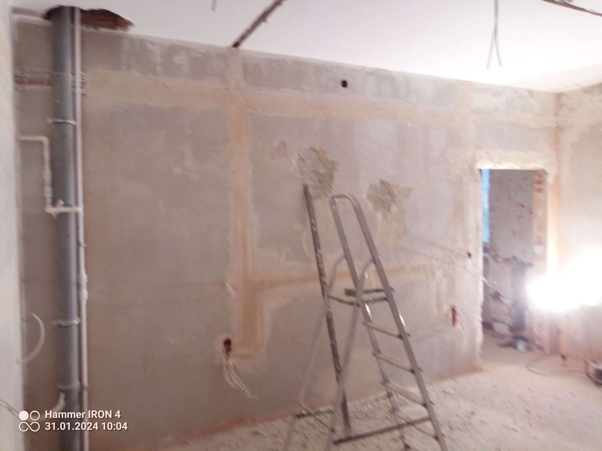 Wnętrze w trakcie remontu: ściana po szpachlowaniu z widocznymi przewodami elektrycznymi, drabina aluminiowa i rury kanalizacyjne przy ścianie.