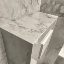 Półka i zabudowa stelaża WC wykończone płytkami imitującymi marmur Calacatta, widoczny biały przycisk spłuczki.