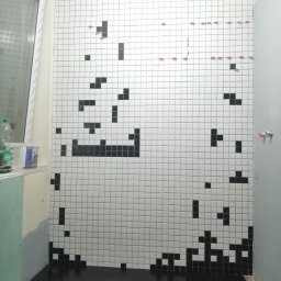SAVCHUK-BUD SPÓŁKA Z OGRANICZONĄ ODPOWIEDZIALNOŚCIĄ - Ściana w łazience w trakcie układania białych płytek z czarnymi akcentami tworzącymi pikselowy wzór, widoczne krzyżyki dystansowe, czarna podłoga, okno w rogu.