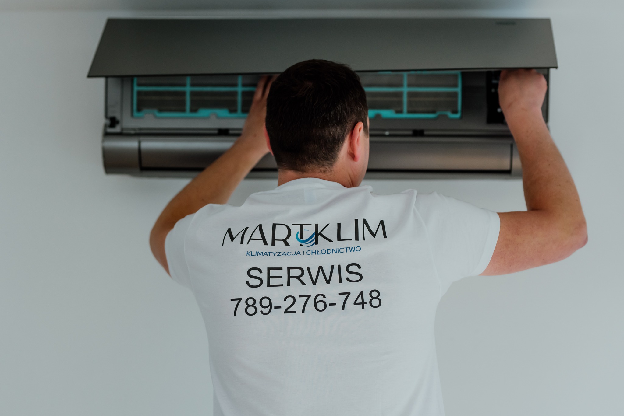Technik w koszulce firmowej MARTKLIM serwisuje klimatyzator ścienny, widoczne filtry i wnętrze urządzenia.