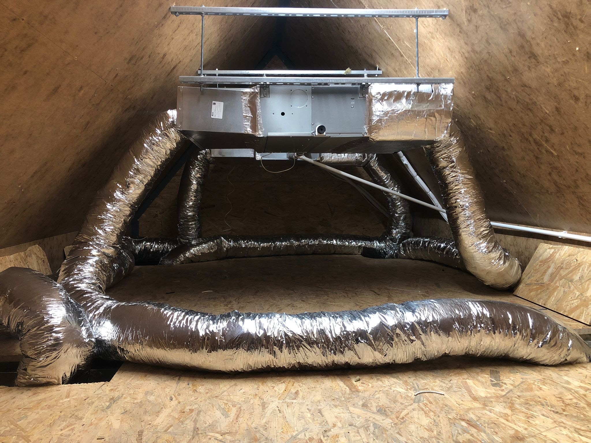 Centralna jednostka klimatyzacji kanałowej z izolowanymi przewodami wentylacyjnymi, zamontowana w przestrzeni poddasza z drewnianym poszyciem.