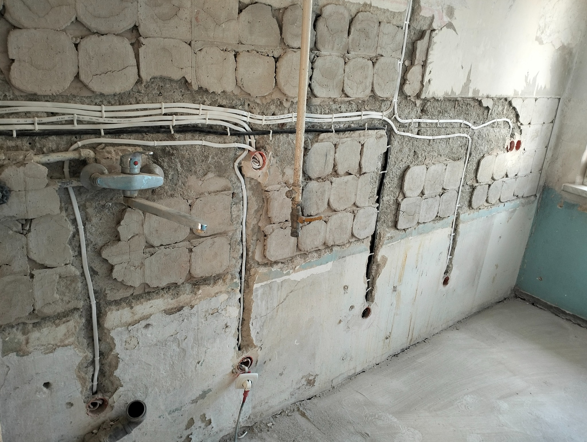 Ściana w trakcie remontu z widocznymi przewodami elektrycznymi, puszkami instalacyjnymi i fragmentem instalacji wodnej z baterią.