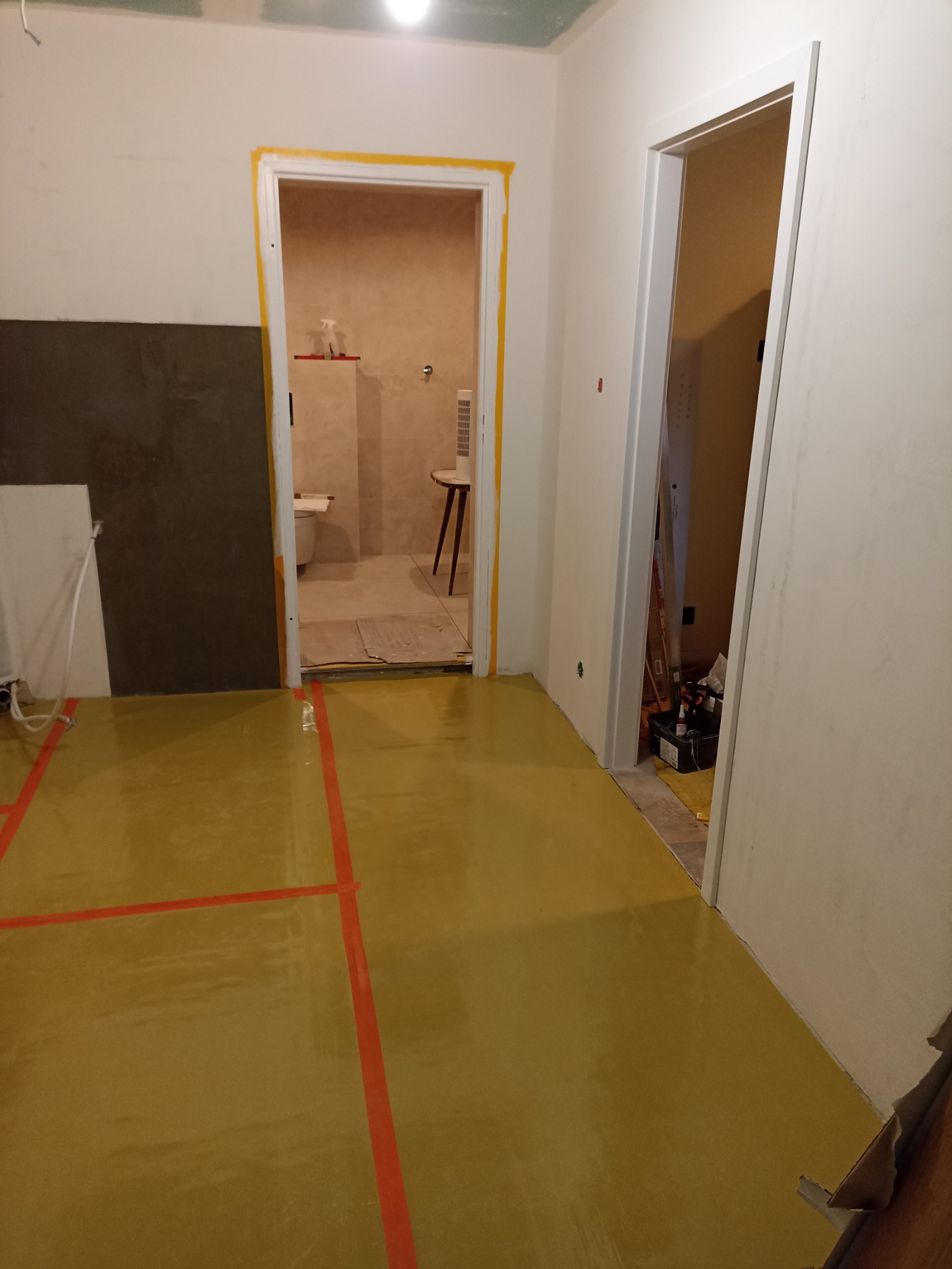 Przygotowanie podłoża pod wylewkę samopoziomującą w trakcie remontu mieszkania, widoczne taśmy wyznaczające obszary, zabezpieczone futryny drzwiowe, fragment łazienki w tle.