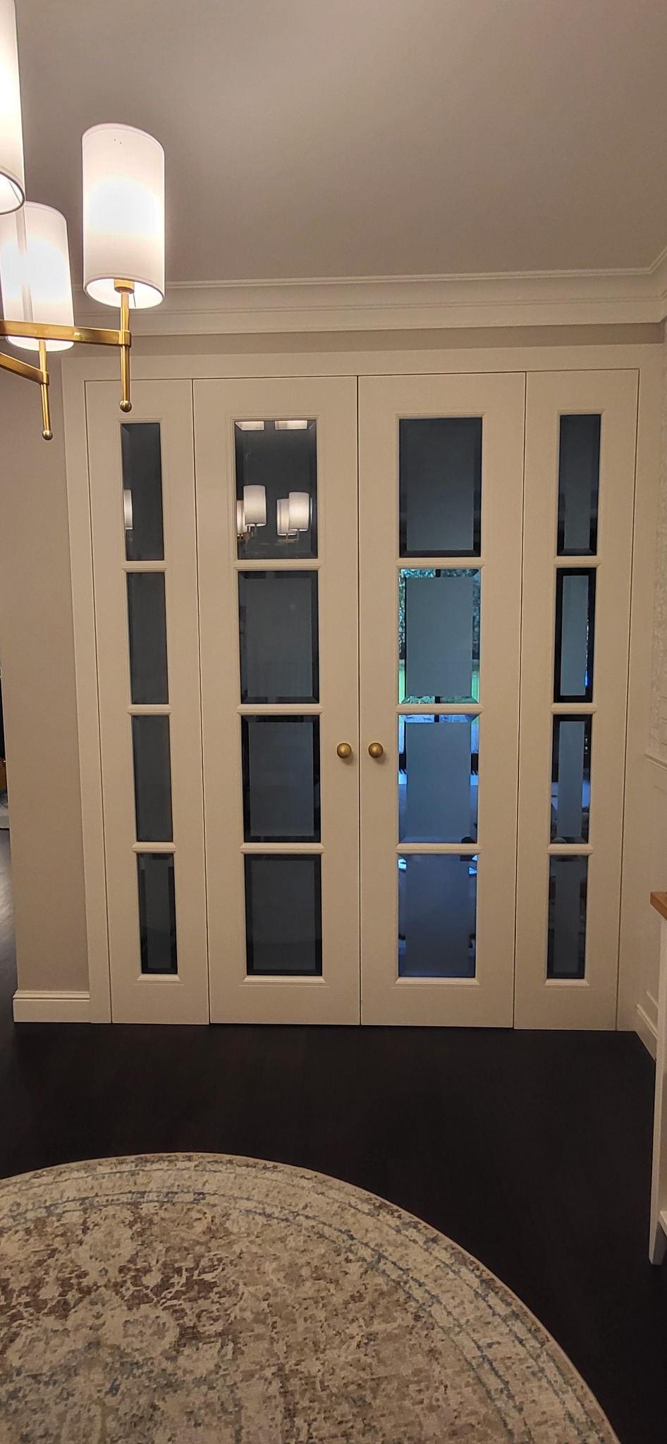 Zamknięte, białe, czteroskrzydłowe drzwi wewnętrzne z prostokątnymi przeszkleniami, widoczne w eleganckim wnętrzu z ciemną podłogą i fragmentem dywanu.