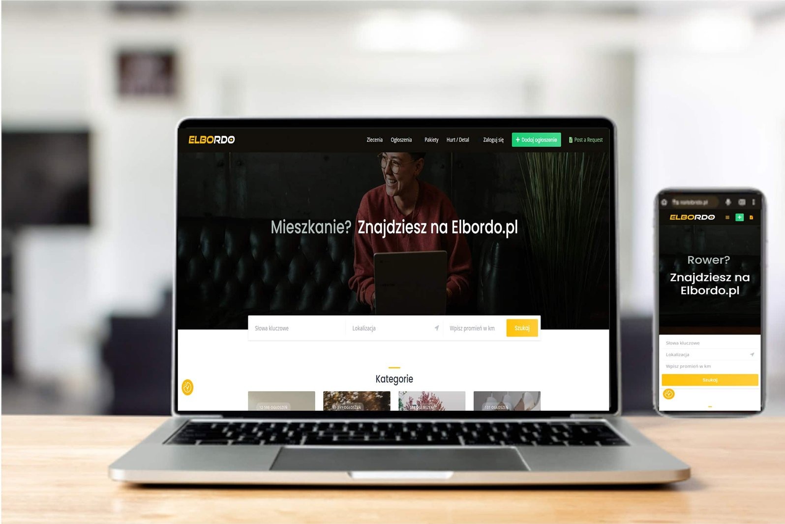 Laptop i smartfon prezentują stronę internetową Elbordo.pl na drewnianym biurku, z widocznym logo i interfejsem. Ekran laptopa jest głównym punktem skupienia.