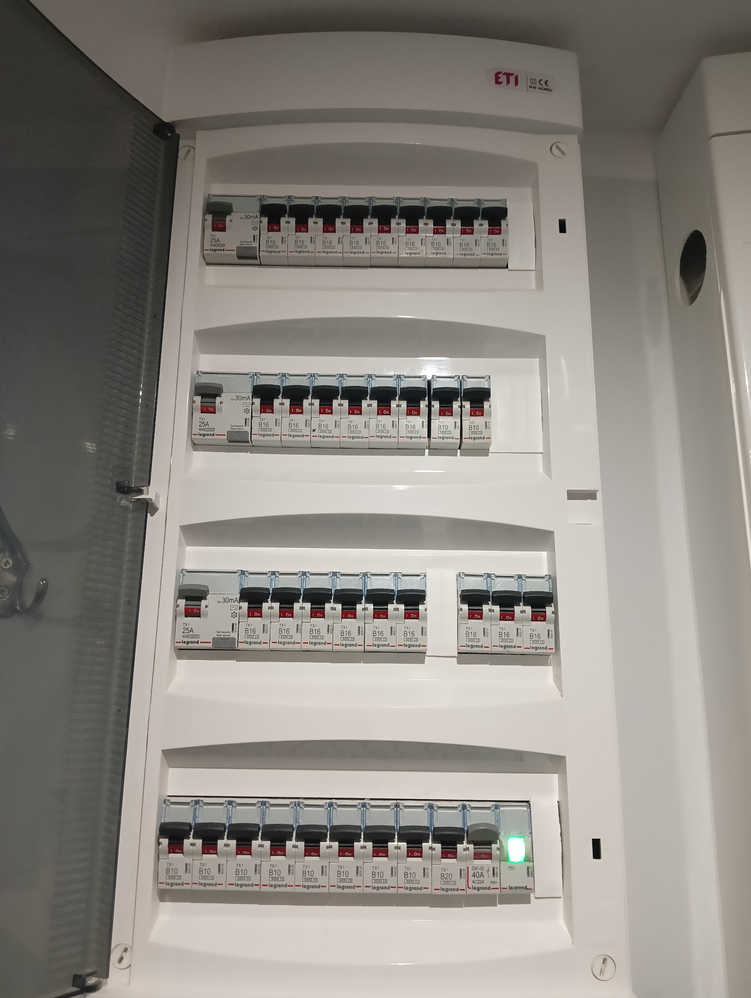 Otwarta skrzynka bezpiecznikowa z zainstalowanymi wyłącznikami Legrand B16 i DX-IS 40A, widoczne oznaczenia i dioda sygnalizacyjna na jednym z wyłączników.