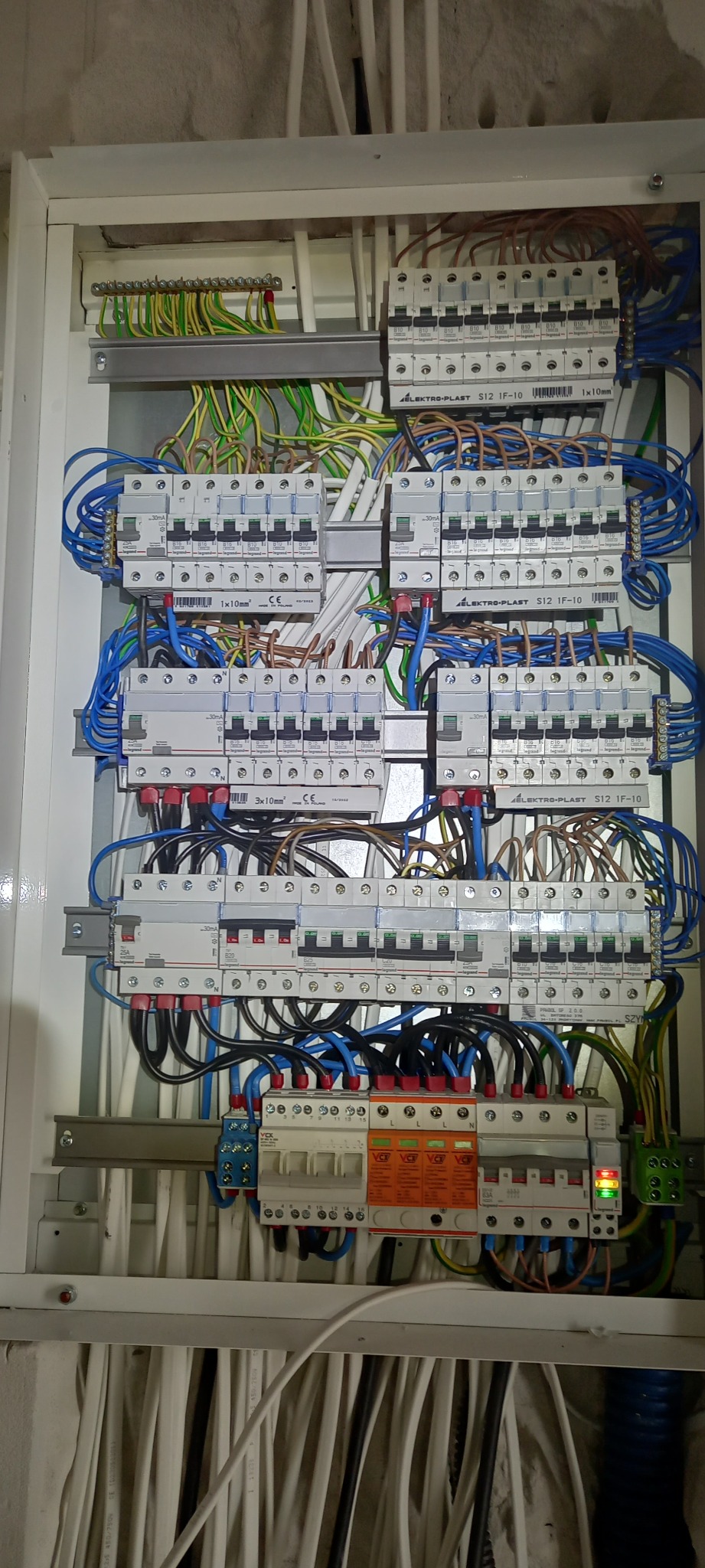 Rozdzielnica elektryczna w białej obudowie z widocznymi bezpiecznikami, przewodami w różnych kolorach i listwami zaciskowymi; widoczne oznaczenia producenta Elektro-Plast.