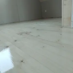 Jasne, lakierowane deski podłogowe w nowym poddaszu z płytami karton-gips na ścianach i drewnianą konstrukcją dachu. Widok z dołu, blisko podłogi.