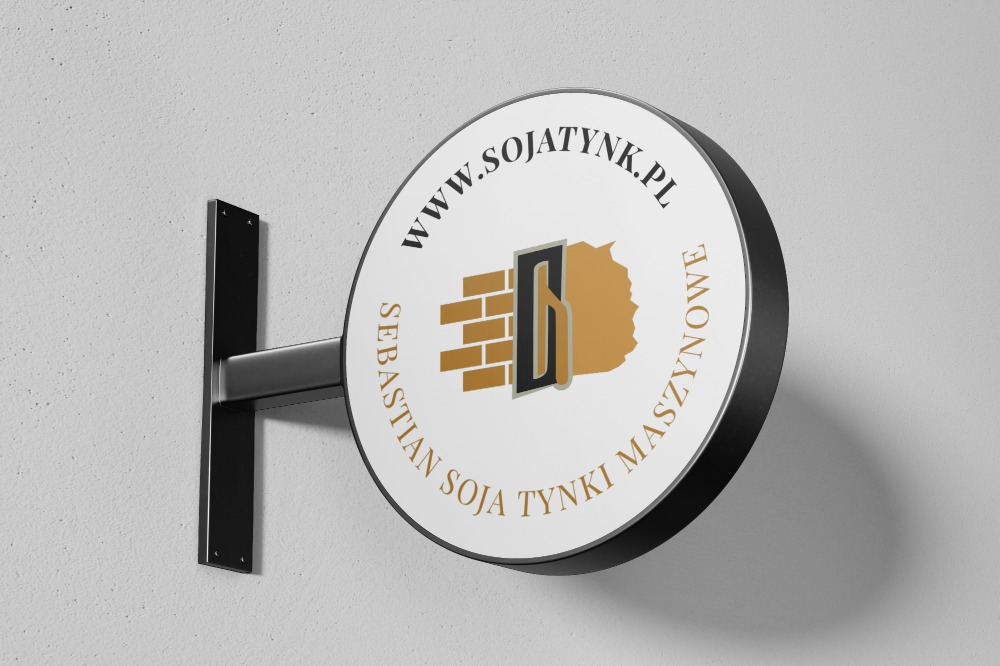 Okrągły szyld reklamowy firmy z branży budowlanej, z logo przedstawiającym mur z kielnią i napisem 'www.sojatynk.pl Sebastian Soja Tynki Maszynowe', zamocowany na ścianie.