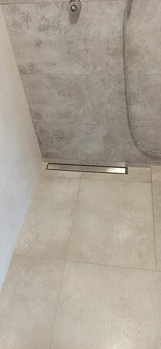 Wykończona strefa prysznicowa z odpływem liniowym, wyłożona płytkami w odcieniach beżu i szarości, widoczna słuchawka prysznicowa.