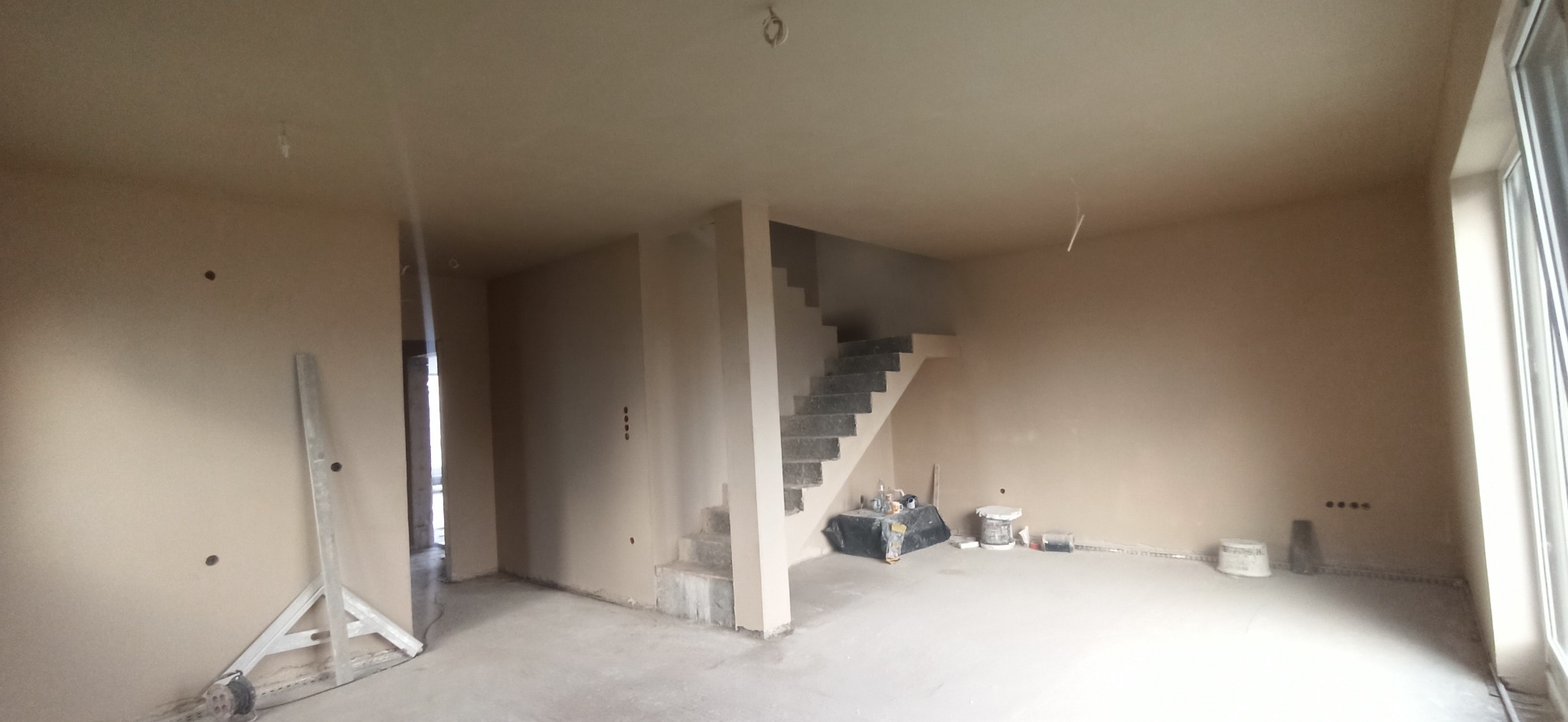Wnętrze domu w Iławie po tynkowaniu, widoczne schody, ściany w jasnym odcieniu, narzędzia pracy i pozostałości po pracach wykończeniowych.
