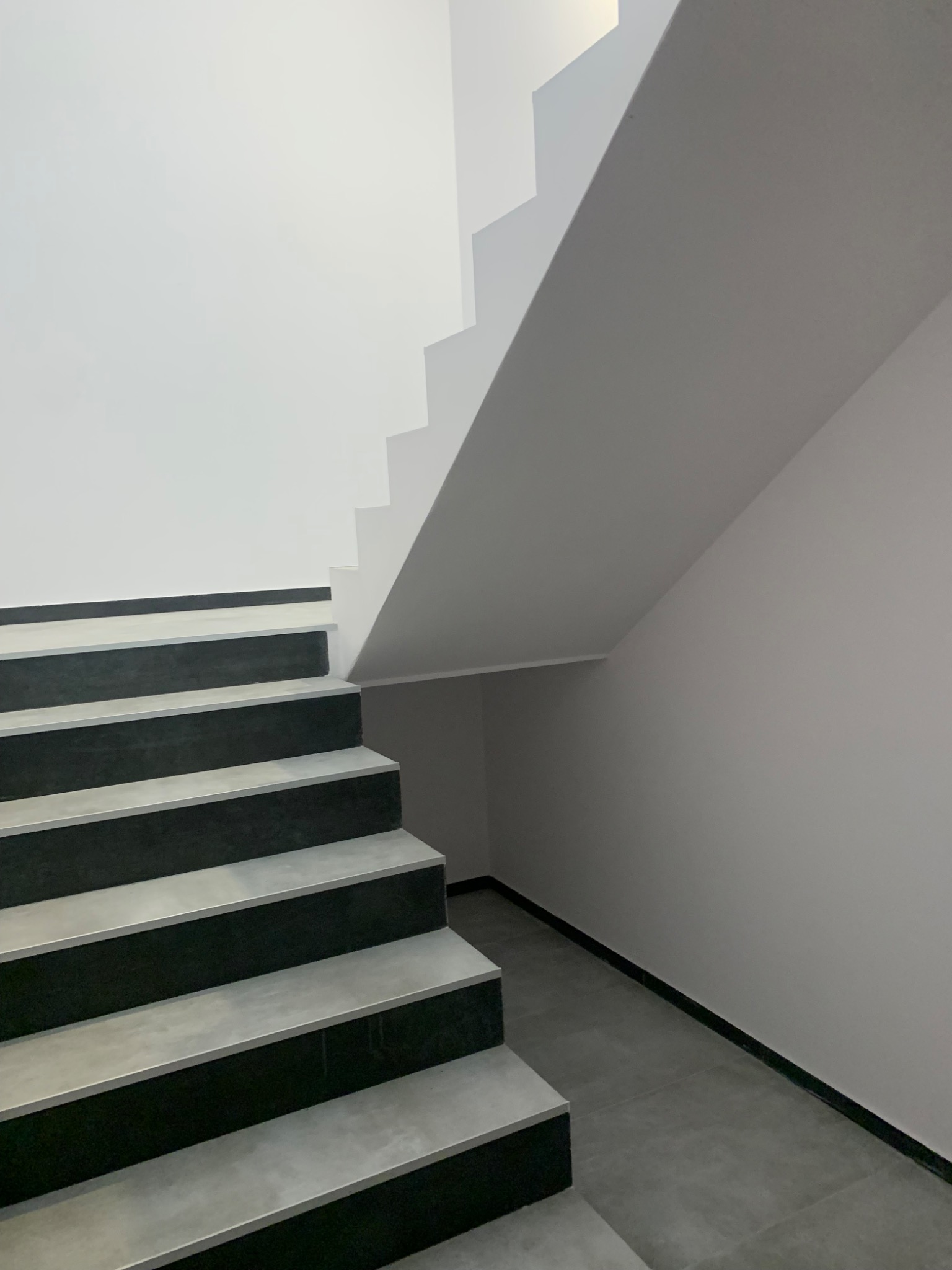 Nowoczesne schody z czarnymi podstopnicami i szarymi stopnicami, białe ściany i szara podłoga, minimalistyczny design.