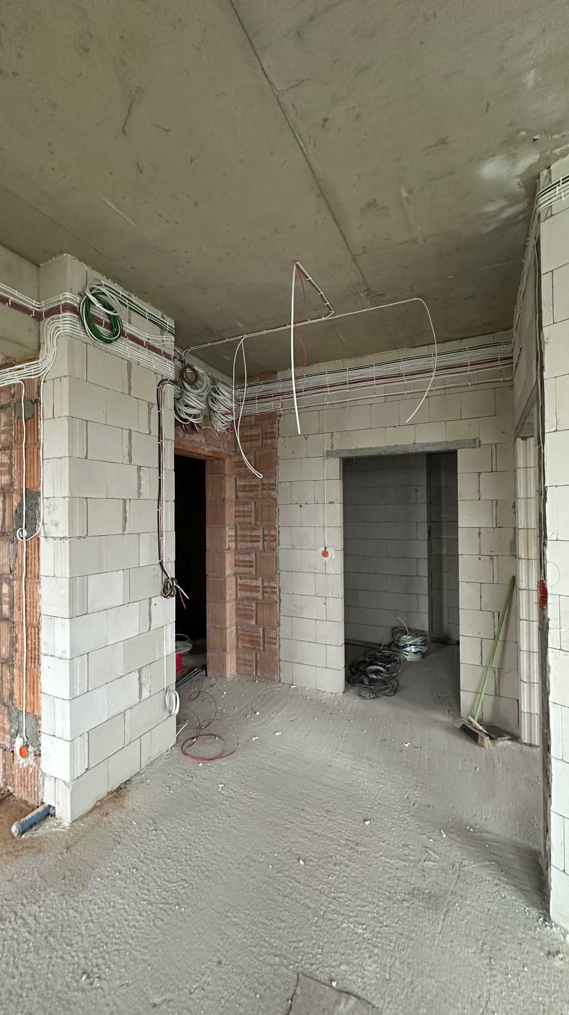 Surowy stan wnętrza z widocznymi przewodami elektrycznymi prowadzonymi po ścianach i suficie, instalacja w trakcie realizacji, ściany z białych bloków, widoczne kable w różnych kolorach.