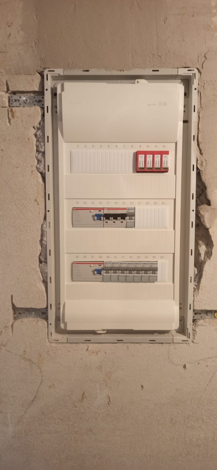 Rozdzielnica elektryczna w obudowie, zamontowana w surowej ścianie, widoczne zabezpieczenia i wyłączniki, w trakcie montażu.