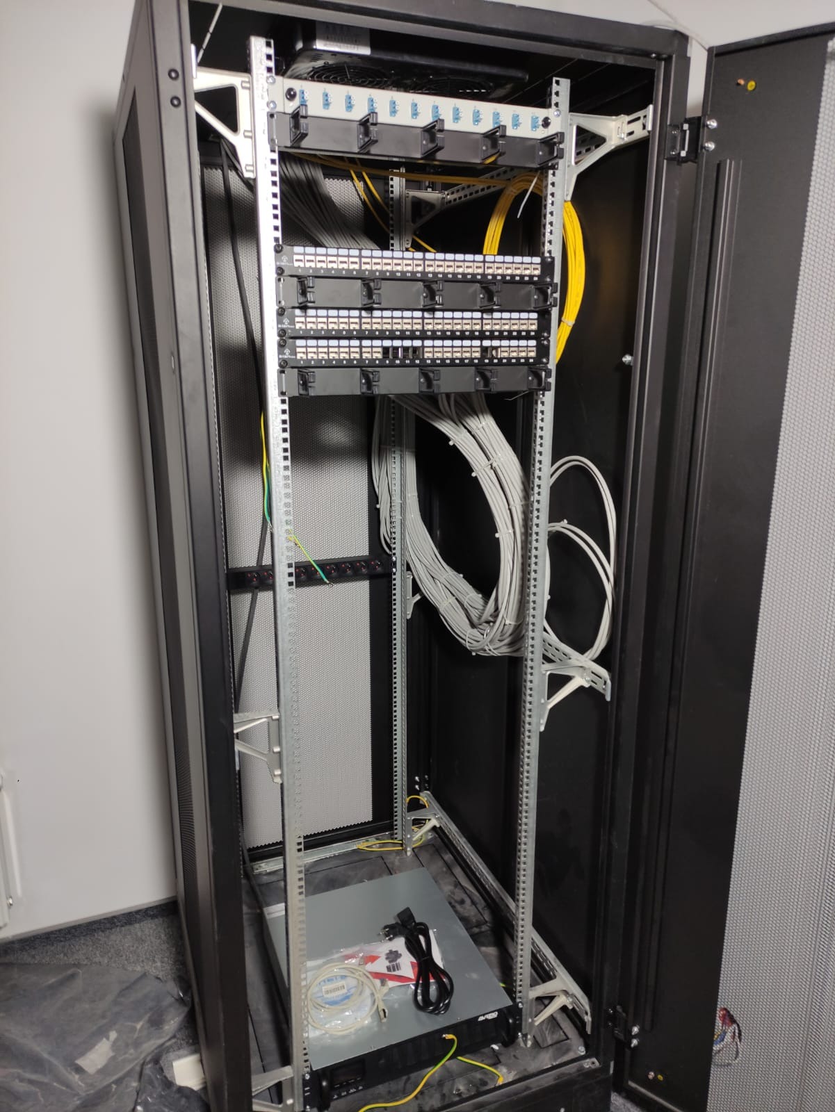 Szafa serwerowa z panelami krosowniczymi i uporządkowanymi kablami sieciowymi w trakcie instalacji w Warszawie, widoczne narzędzia i akcesoria na dnie szafy.