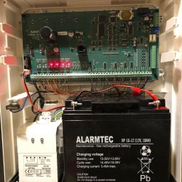 Balex electro - Wnętrze obudowy alarmowej z płytą główną, transformatorem i akumulatorem ALARMTEC BP 18-12, widoczne czerwone diody LED.