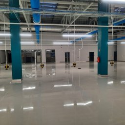 Balex electro - Wnętrze hali produkcyjnej z widoczną instalacją elektryczną pod sufitem, niebieskie rury wentylacyjne, oświetlenie LED i słupy pomalowane na niebiesko.