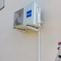 Wen-tech - Biały klimatyzator Haier zamontowany na beżowej ścianie budynku, widoczna drabina aluminiowa z naklejkami.