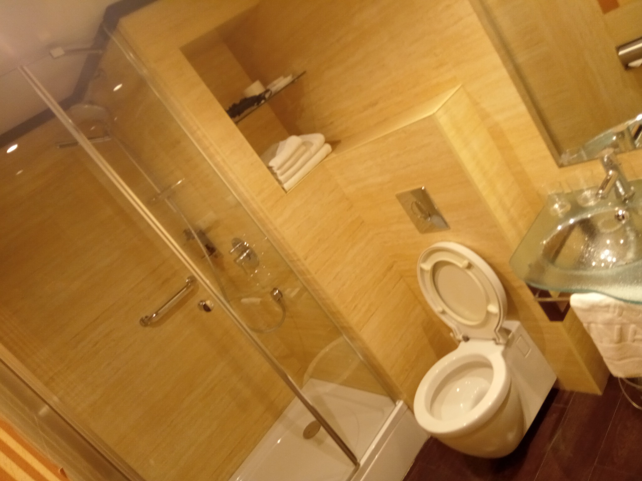 Nowoczesna łazienka w odcieniach beżu z kabiną prysznicową ze szklanymi drzwiami, wiszącą toaletą i umywalką nablatową ze szklanym blatem.