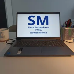 Laptop Lenovo z wyświetlonym logo firmy księgowej 'SM Biuro Rachunkowe PASJA Szymon Mońko' na biurku z kubkiem i przyborami biurowymi.