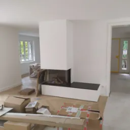 Wnętrze w trakcie prac wykończeniowych, z nowoczesnym kominkiem obudowanym białą konstrukcją z czarnym blatem, kartony i narzędzia na podłodze z jasnego drewna, widok na kolejne pomieszczenia przez...