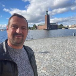 JiM MALERI - Mężczyzna w skórzanej kurtce robi selfie na tle Ratusza w Sztokholmie i rzeki Mälaren w słoneczny dzień.