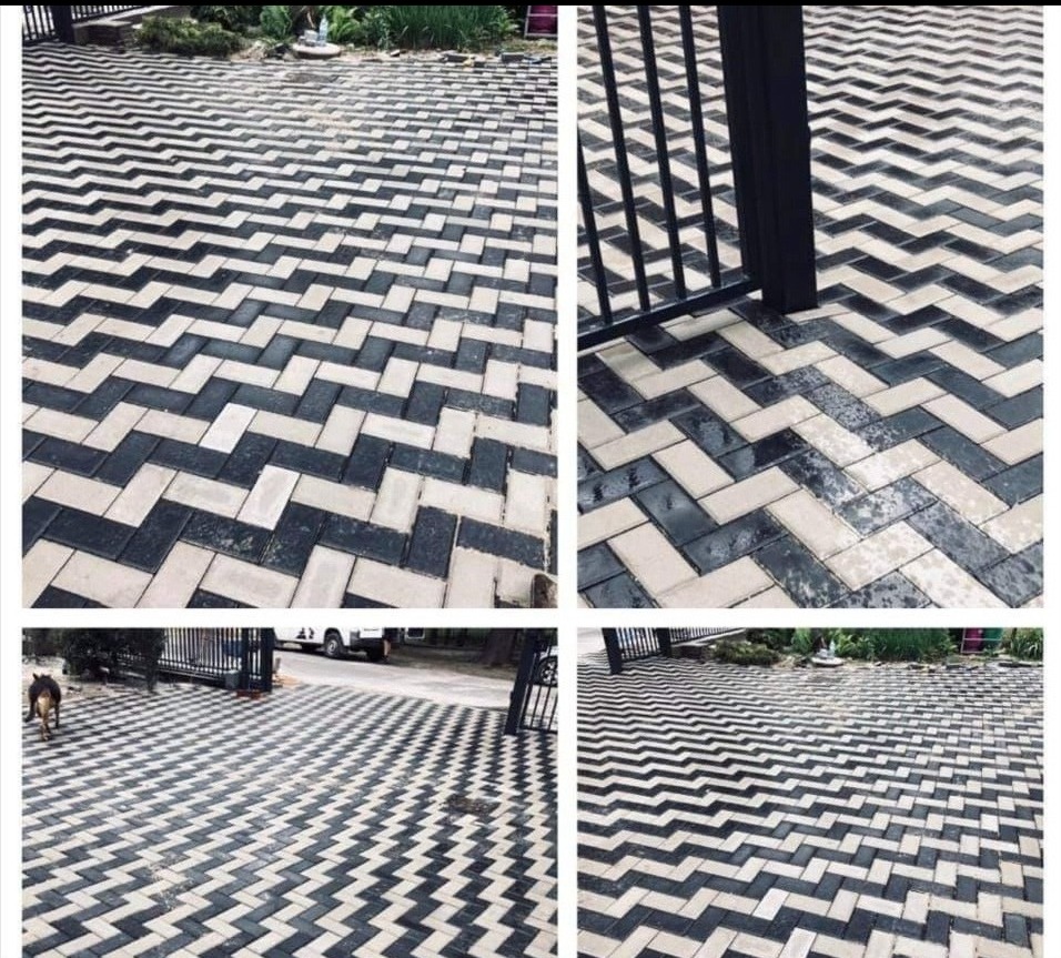 Ułożona w zygzak wzór z ciemnych i jasnych betonowych kostek na podjeździe, widoczna brama w tle i fragment samochodu.