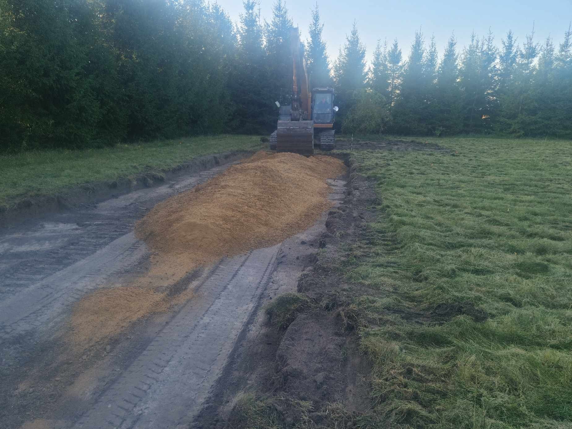 Koparka gąsienicowa Case na skraju wykopu z nasypanym piaskiem na tle lasu iglastego.