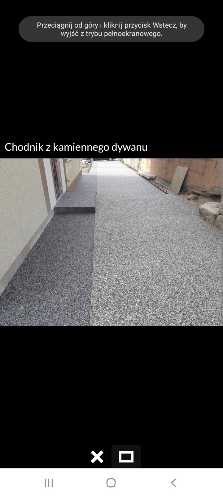 Chodnik z kamiennego dywanu w odcieniach szarości, ułożony przy ścianie domu z widocznymi schodami wejściowymi, z elementami wykończeniowymi i fragmentami otoczenia.