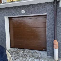 NA PILOTA ŁUKASZ ZAJĄKAŁA - Brązowa brama garażowa segmentowa Hormann z poziomymi przetłoczeniami, widoczna z boku, z fragmentem zaparkowanego samochodu i zaśnieżonym podjazdem.